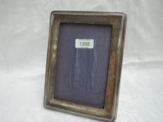 A silver photograph frame of plain rectangular form having a wooden back with easel stand and blue