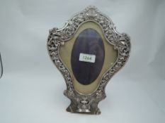 A Victorian silver photograph frame of cartouche form having a silver border with scroll, cherubic