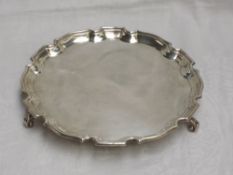 A silver salver of plain circular form having an indented pie crest rim and trefoil scroll feet,