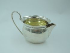 A small Edwardian silver cream jug of oval form having frilled rim, looped wire handle and gilt