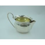 A small Edwardian silver cream jug of oval form having frilled rim, looped wire handle and gilt