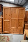 A modern pine triple wardrobe with part drawer base