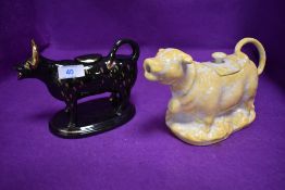 Two ceramic creamers in the form of cows one black and one yellow glazed