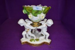 A porcelain table center by T. Goode and Co, London three cherubs holding lily dish on Greek key