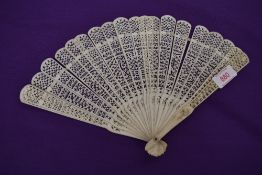 An intricate antique fan having carved ribs and mother of pearl rivet.