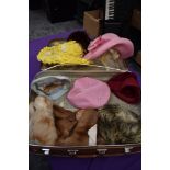 A suitcase containing an assortment of vintage hats and a fur stole, various eras and styles.