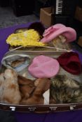 A suitcase containing an assortment of vintage hats and a fur stole, various eras and styles.