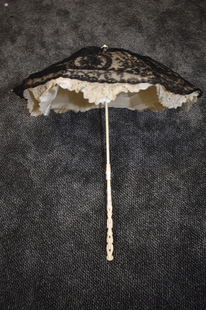 A Victorian parasol having fine black lace over cream tatting and silk ground,white carved handle