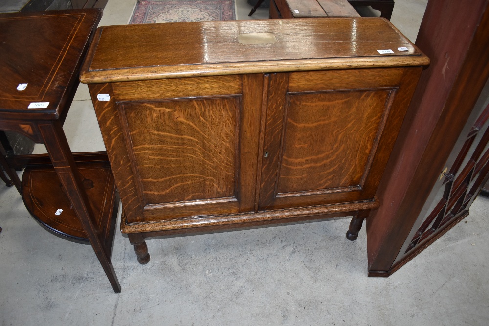 An early 20th Century oak cabinet of slender form having lift flap top and double cupboard doors,