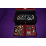 A vintage black jewellery case containing a selection of costume jewellery including brooches,