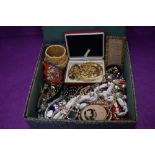 A material covered box containing a selection of costume jewellery including gold plated items,