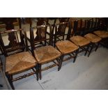 A set of six rail back dining/kitchen chairs having rush seats and a further rocking chair of
