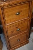 A rustic pine filing cabinet having three drawers