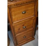 A rustic pine filing cabinet having three drawers