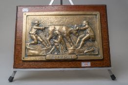 A metal plaque having raised scene depicting three men and a bull titled 'The law suit' mounted on