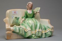 A katzhutte figurine of lady on sofa holding a fan with bonnet by her side in green and yellow