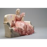 A katzhutte figurine of lady on sofa holding a fan with bonnet by her side in a pink period costume,
