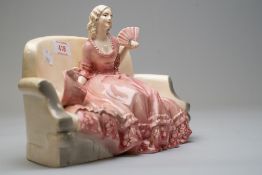 A katzhutte figurine of lady on sofa holding a fan with bonnet by her side in a pink period costume,