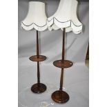 A pair of traditional oak standard lamps with integral side tables, having turned frames