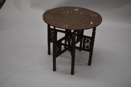 An Indian brass top folding table having fretwork and carved turned frame and detailed decoration to