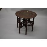 An Indian brass top folding table having fretwork and carved turned frame and detailed decoration to