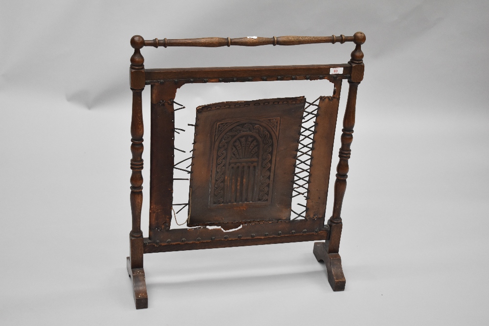 An early 20th Century firescreen having turned oak frame and tooled leather panel and strap work