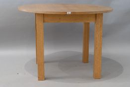 A modern circular golden oak dining table , having integral leaf extension on square chunky legs,