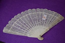 An intricate antique fan having carved ribs and mother of pearl rivet.