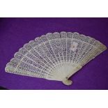 An intricate antique fan having carved ribs and mother of pearl rivet.