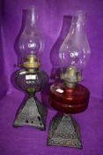 Two Victorian oil burning lamps having decorative cast bases with red and green oil wells