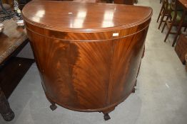 An early 20th Century mahogany demi lune side cabinet having flame mahogany doors, short cabriole