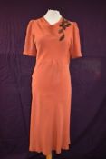 A 1930s art deco coral coloured crepe day dress having cowl neck and appliqué flower detail to