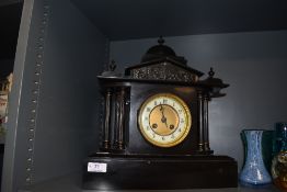 An antique chiming mantle clock of black polished stone having painted metal columns to sides,