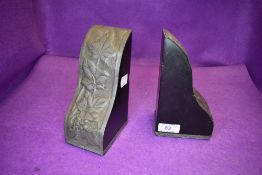 A pair of ebonised bookends in the arts and crafts style having raised metal work cladding to