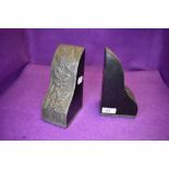 A pair of ebonised bookends in the arts and crafts style having raised metal work cladding to