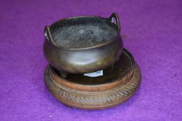 A Chinese bronze effect incense bowl with wooden stand having character seal marks to base