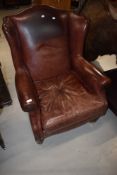 A pair of reproduction wing back armchairs in brown leather
