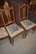 A pair of early 20th Century oak dining chairs having shaped slat backs, drop in woolwork seats