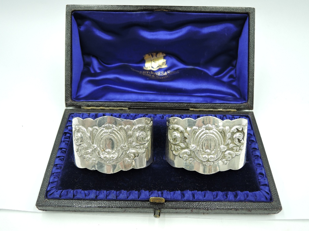 A cased pair of Victorian silver napkin rings of oval cuff form having repousse decoration to