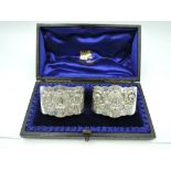 A cased pair of Victorian silver napkin rings of oval cuff form having repousse decoration to