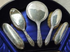 A cased five piece silver dressing table set having leaf and berry decoration to borders, Birmingham