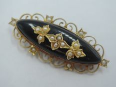 A Victorian black onyx oval mourning brooch having seed pearl decoration in a yellow metal