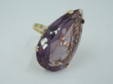 An over sized synthetic alexandrite pear shaped solitaire ring in a 4 claw set yellow metal basket