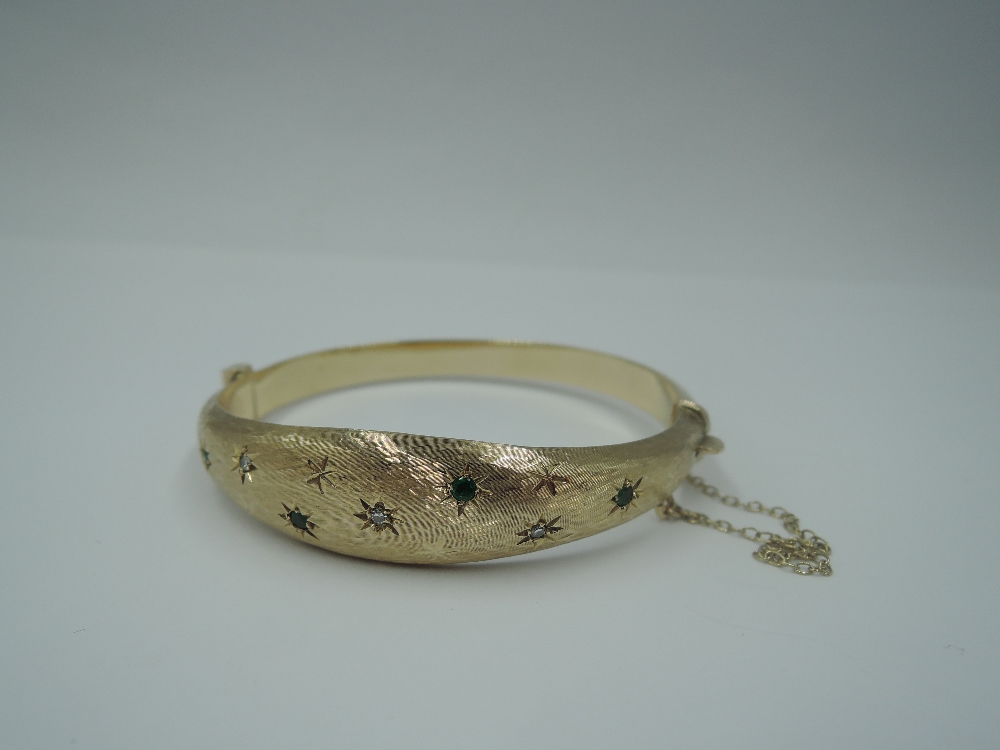 A 9ct gold hinged bangle having diamond and emerald chip decoration in star burst settings on