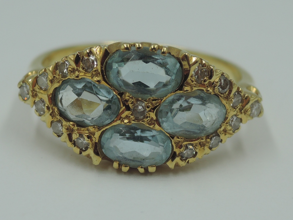 An aqua marine dress ring having four oval stones in a lozenge shaped panel with diamond chip