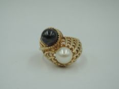 A yellow metal dress ring stamped 14K having a duo of black and white cultured pearls in a raised