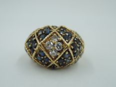 A yellow metal dress ring of domed form having extensive sapphire and diamond decoration in a