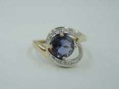 A 9ct gold dress ring having a blue paste central stone within diamond chip set swirl shoulders on a