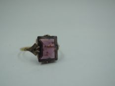 A yellow metal dress ring stamped 9ct having a rectangular purple paste stone in a claw set mount,