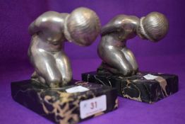 A pair of art deco book ends on marble bases of two nude kneeling ladies